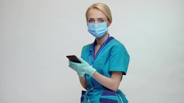 Medical Doctor Nurse Woman Wearing Protective Mask and Latex Gloves - Using Mobile Phone