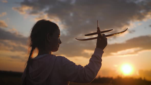 Silhouette Little Girl Playing with Airplane on a Field During Sunset. Concept Big Child Dream. alt