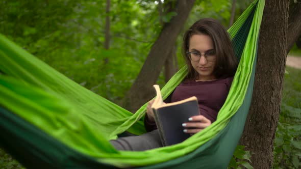 A Young Woman Lies in a Hammock and Reads a Book