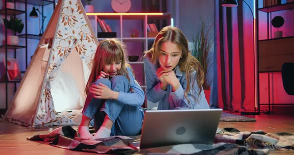 girls watching scary movie on laptop,one of them closed eyes from scare while another attantivly