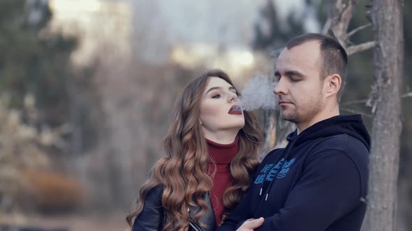 beautiful girl smokes an electronic cigarette blowing smoke at her boyfriend. a pair of millennial