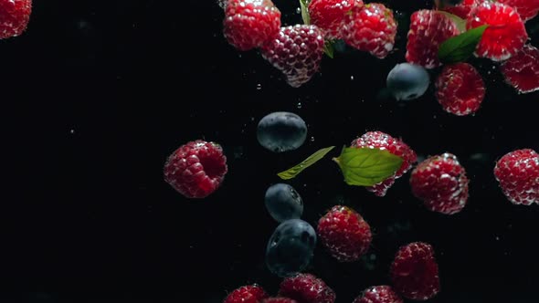 Fresh Raspberries with Blueberries and Fresh Mint Leaves Fall on a Black Background Into the Water