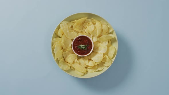 Close up of potato chips in a bowl with sauce on blue surface