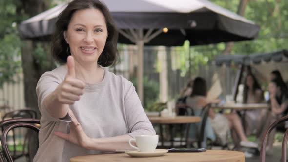 Thumbs Up by Old Woman Sitting in Outdoor Cafe