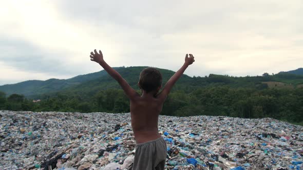 Poverty Boy Standing On Garbage Dump With Arms Raised