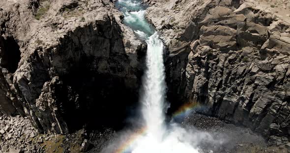 Aerial view of a crane shot of a powerful waterfall that generates a rainbow as it falls by the acti