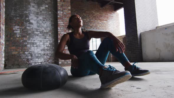 African american man sitting resting after exercising with medicine ball in an empty urban building