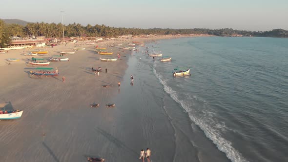 Tourists strolling along the golden sand near the coastline with moored fishing boats, Palolem Beach