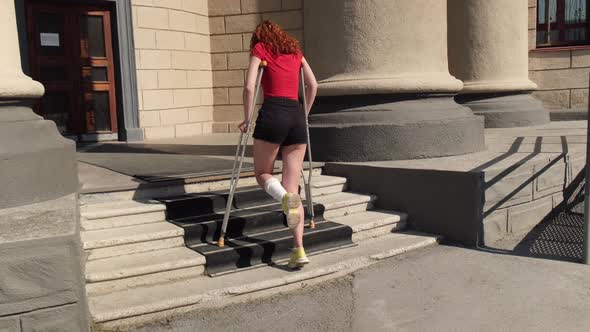 Young Redhaired Woman with Ankle Injury Climbs Stairs on Crutches