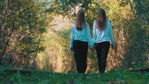 Twins Girls Holding Hands Walking Along Railroad Tracks. Back View. Slow Motion