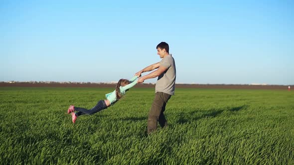 Young Father in Casual Spinning His Daughter in Circles Playing Having Fun in Nature on a Bright Day