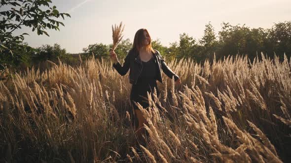 Beautiful Young Woman in the Field Spins with Flowers and Spikelets