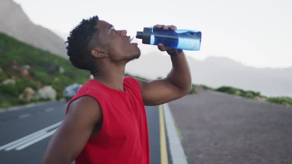 African american man drinking water while standing on the road