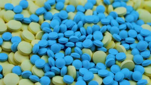 Bright Blue and Yellow Small Round Vitamins Lie on the Table and Rotate.