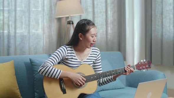 Asian Woman Having Video Call On Laptop And Playing A Guitar At Home