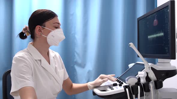 A Female Doctor in Mask and Gloves Looks at the Ultrasound Screen in a Modern Clinic