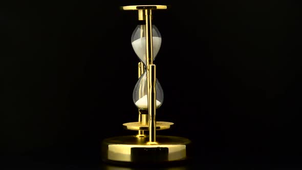 Vintage Hourglass with White Sand Pouring Rotation. Black Background