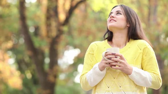 Woman in sweater hold cup of drink in autumn park