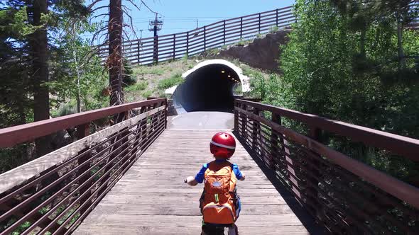 A boy rides his mountain bike through a tunnel on a paved trail in the woods.