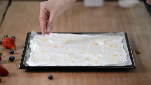 A professional pastry chef makes a meringue roll, sprinkle almonds flakes on the base