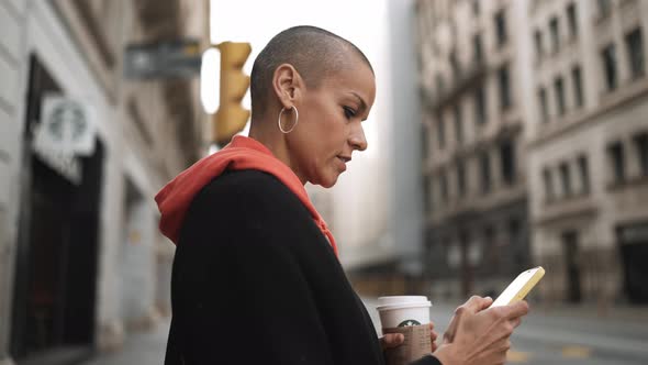 Serious bald woman texting by smartphone and walking