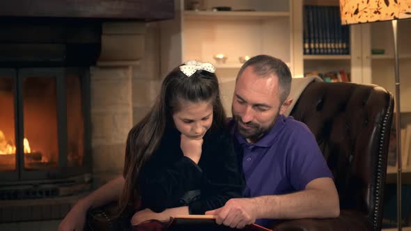 Dad Reading His Little Princess a Fairy Tale Near the Fireplace in the Evening