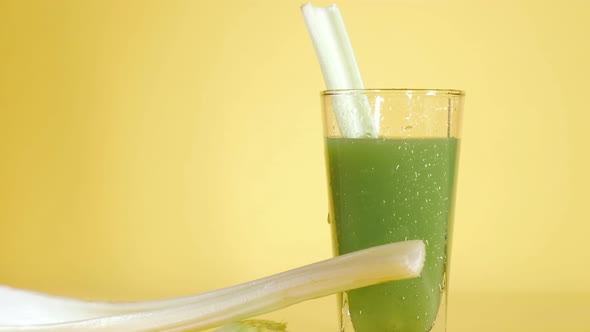 Delicious organic celery juice in a glass on a yellow colored background.