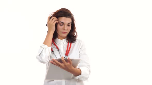 Friendly Young Female Doctor Reviews and Writes Notes on a Clipboard