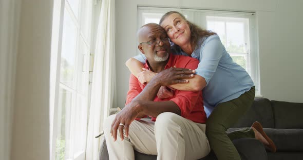 Happy senior diverse couple wearing shirts and embracing in living room