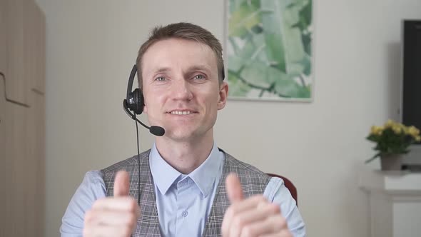 Young Businessman Communicates By Video Link Smiles and Raises His Thumbs Up