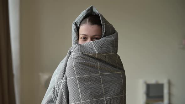 smiling and funny woman wrapped in a blanket in the morning after waking up