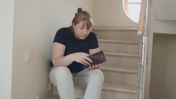 A Caucasian woman is sitting on the stairs and cannot find money in her wallet.