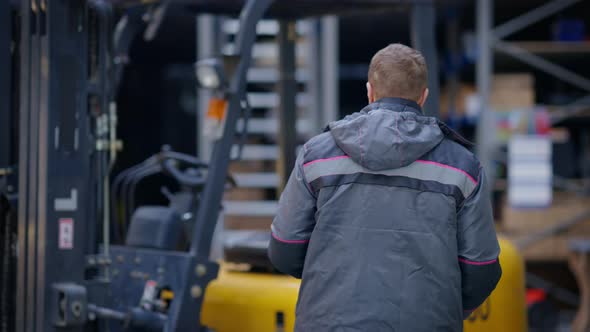 Male Caucasian Worker Filling in Documents and Walking to Forklift Sitting on Driver's Seat