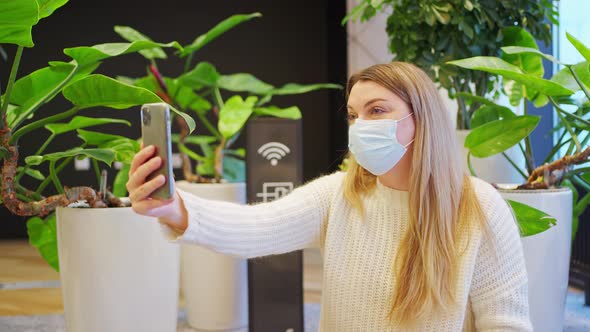 a Woman in a Protective Mask is Talking on a Video Link Next to a Wifi Sign and Next to Green Plants