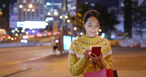 Woman holding with shopping bag and use of mobile phone in city at night