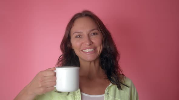 Smiling Cheerful Woman Hold Hot Cup of Coffee or Tea Isolated on a Pink Color Background