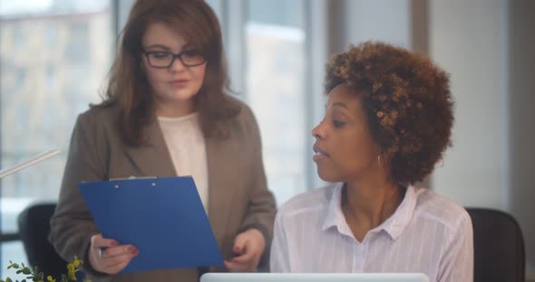 Young African Businesswoman Working on Computer with Colleague Showing Her Clipboard with Documents