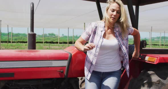 Video of happy caucasian woman standing in front of tractor