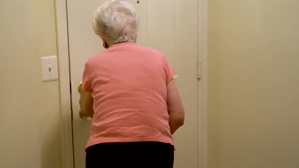 Elderly woman uses can to walk to door, opens door and welcomes home healthcare nurse.