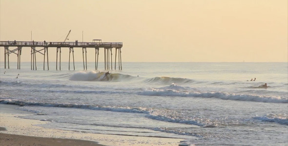 Surfers Catching Waves Near Pier at Sunrise