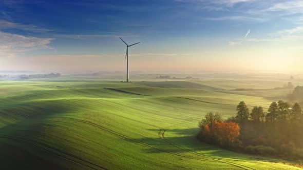 Stunning foggy wind turbine on green field at sunrise