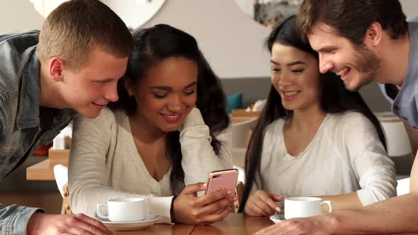Four Friends Watch Something on Smartphone at the Cafe