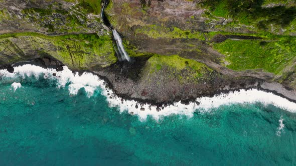 Bride's Veil falls from vertical cliffside onto rocky coastline, Madeira; drone