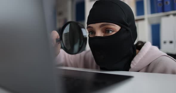 Internet Theft and Persons in Balaclava with Magnifying Glass Behind Laptop