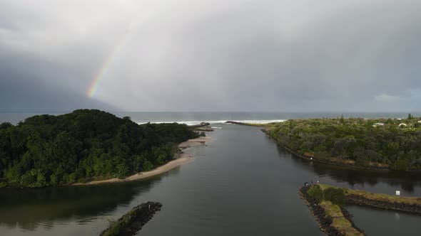 High static drone view of a large rainbow on a sunny day with scenic outlook towards a river mouth l