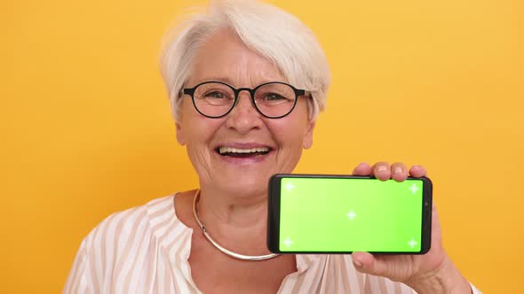 Old Smiling Woman Showing the Smartphone. Green Screen for Replacement