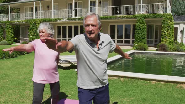 Happy caucasian senior couple practicing yoga in garden standing and stretching in the sun