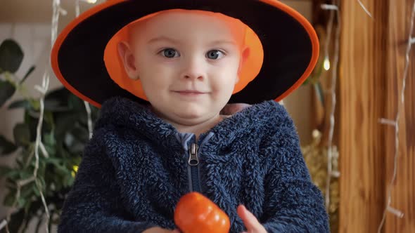 Portrait of Baby Boy Wearing Halloween Hat and Holding Little Pumpkin