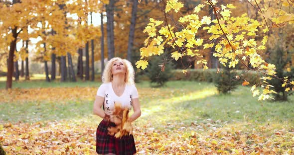 Happy Blonde Woman in Sexy Crop Top and Skirt Playing with Foliage in Park