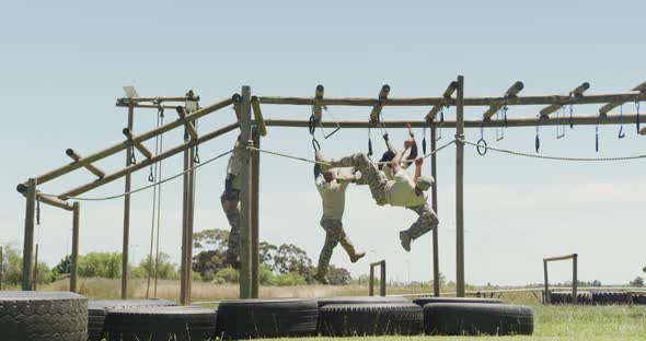 Fit diverse group of soldiers using hanging rope and rings on army obstacle course in the sun alt